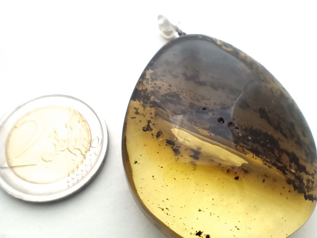 Tikiwe Bernsteinschmuck Größenverhältnis
großer gelb-schwarzer Tropfen aus Bernstein mit einer schräg verlaufenden Banderole aus Einschlüssen, fast wie die Ringe des Saturn Tikiwe Bernsteinschmuck