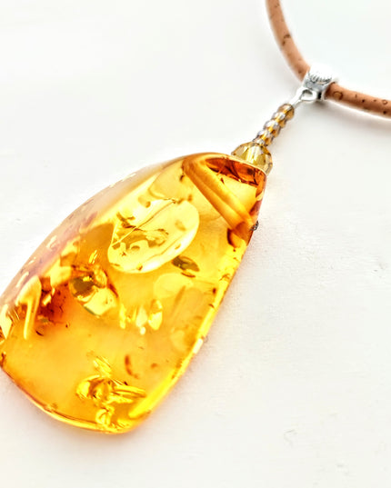 Nahaufnahme des polygonalen, honigfarbenen Bernsteinanhängers mit zauberhaften Einschlüssen. Handmade by Tikiwe-Taschen aus Kork