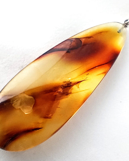 Tikiwe Bernsteinschmuck langer, schmaler Tropfen aus Bernstein, gelblich und bräunlich getigert und hat einen zarten weiteren Einschluss im unteren Bereich, fast wie eine Blume, die je nach Lichteinfall sichtbar ist oder nicht, Öse Sterlingsilber