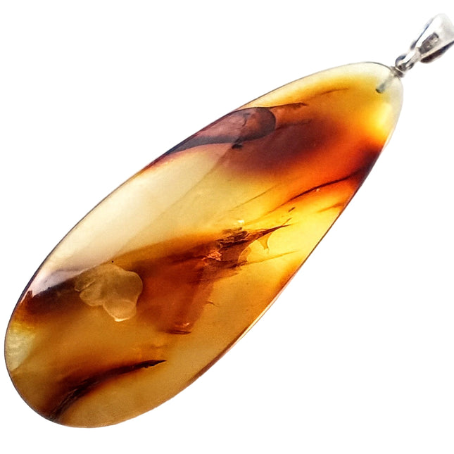Tikiwe Bernsteinschmuck langer, schmaler Tropfen aus Bernstein, gelblich und bräunlich getigert und hat einen zarten weiteren Einschluss im unteren Bereich, fast wie eine Blume, die je nach Lichteinfall sichtbar ist oder nicht, Öse Sterlingsilber