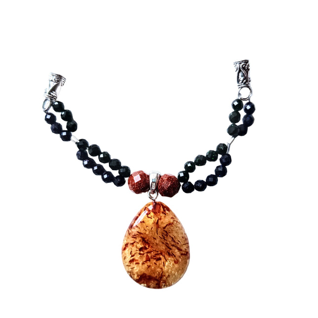 Tropfen aus Bernstein mit Einschlüssen wie Samen?!? Gerahmt von facettierten Kugeln aus Gold-, Blau- und Grünfluss an einer Kordel aus Kork. Made by Tikiwe-Taschen aus Kork